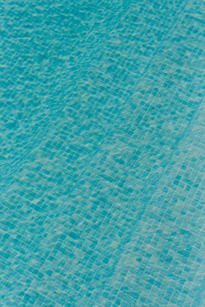 gallery-1 A close-up view of blue mosaic tiles in a swimming pool, capturing sunlight reflections.
