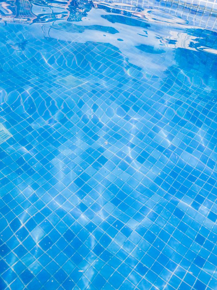 hero-img-02 Close-up of vibrant blue pool tiles under clear water, reflecting sunlight for a refreshing summertime vibe.