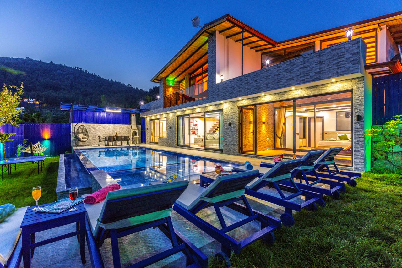contact-img Beautiful modern villa with a well-lit swimming pool and deck chairs in a serene outdoor setting.