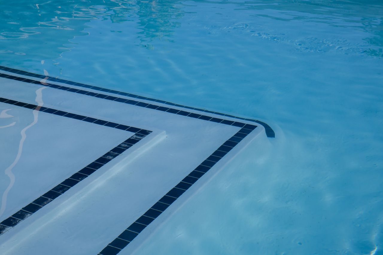 gallery-3 Serene view of a clear blue swimming pool with tiled steps and shimmering water.