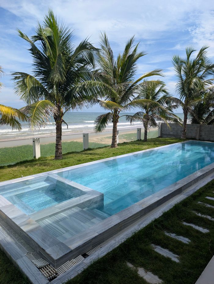 services-02 Stunning coastal view with a modern pool and palm trees beside a sandy beach.