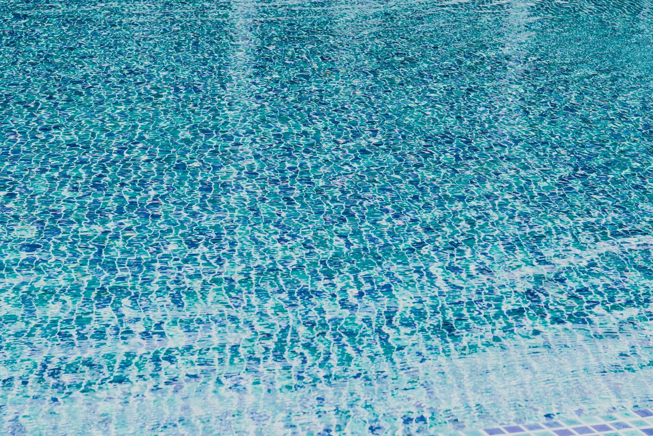 gallery-4 A close-up view of a swimming pool water surface with vibrant blue tiles creating a wavy pattern.