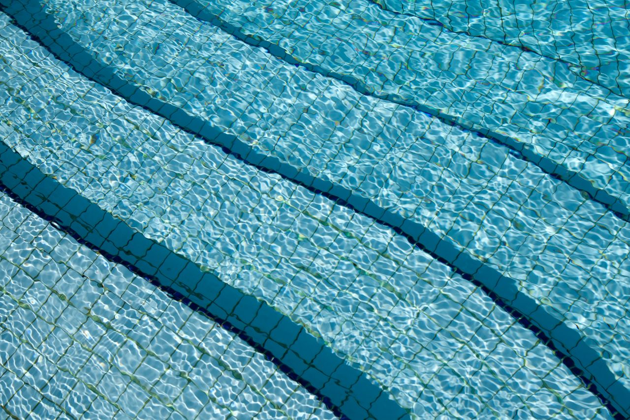 hero-img-01 A detailed view of crystal clear swimming pool water over a tiled surface, showcasing its calm and refreshing nature.